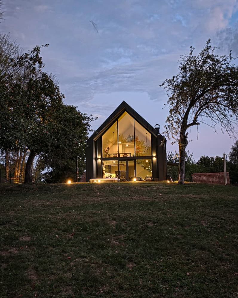 The villa glowing at dusk, seen from across the meadow
